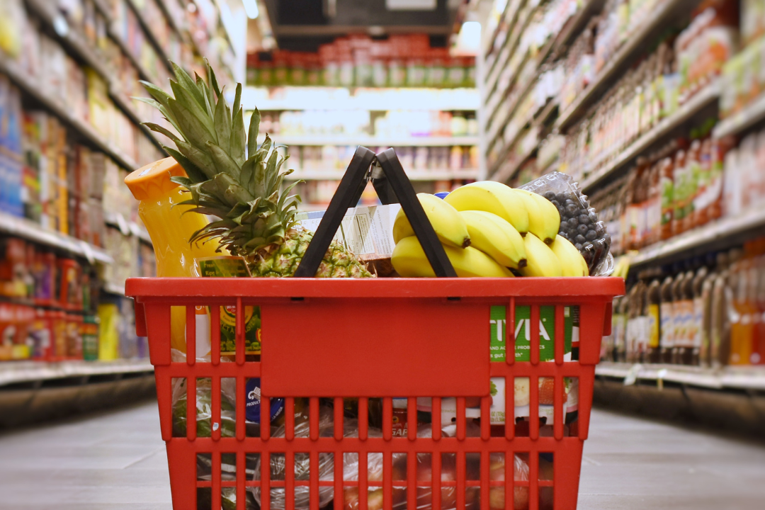 Shopping basket filled with groceries sitting in the middle of the supermarket isle.