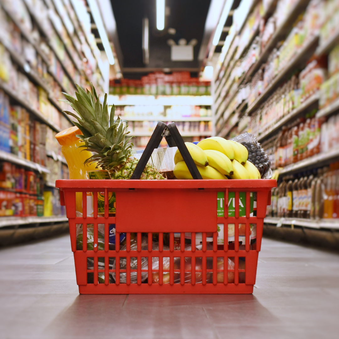 Shopping basket filled with groceries sitting in the middle of the supermarket isle.